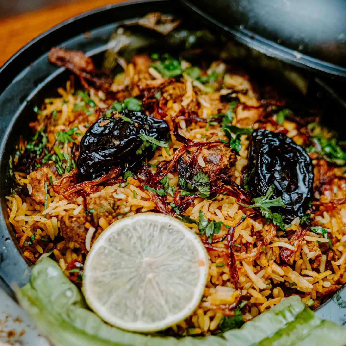 A dum biryani served unmixed, the rice visibly layered with birista, coriander and lime